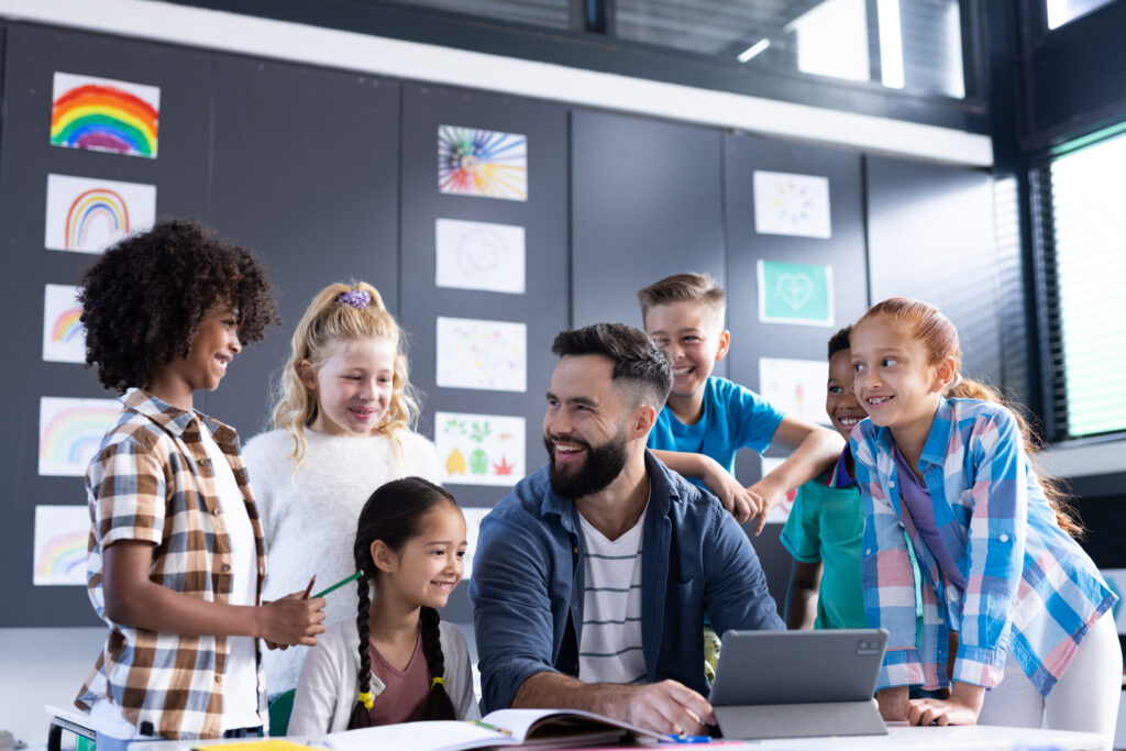 Diverse, happy elementary school children and male teacher positive school culture concept