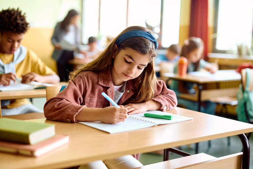 Elementary student writing in her notebook on a class at school.